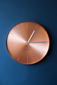 a copper clock with white hands on a blue wall