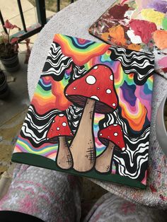 someone is holding up a colorful mushroom painting