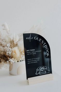 a white vase filled with dried flowers next to a black and white guest book sign