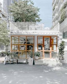 a small white building with lots of windows and plants in front of it on the sidewalk