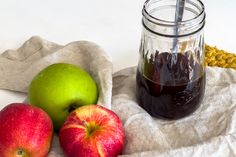 two apples and an apple cider sitting on a cloth next to a jar of liquid