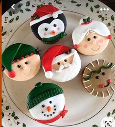 four decorated cupcakes sitting on top of a plate with santa claus and snowmen