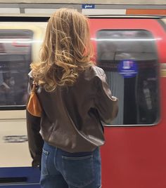 a woman standing in front of a train at a subway station with her back to the camera