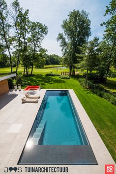 an empty swimming pool in the middle of a lush green yard with lounge chairs around it