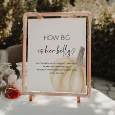 a sign that says how big is her belly? on top of a table with flowers