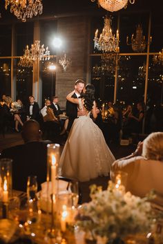 a bride and groom dance at their wedding reception in front of an elegant chandelier