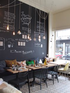 a chalkboard wall in a restaurant with tables and chairs around it that has writing on the walls