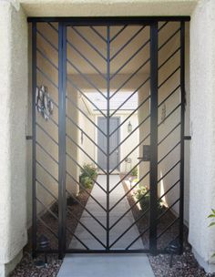 an entrance to a home with black iron doors and decorative plants on the side walk