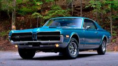 a blue muscle car parked in front of some trees