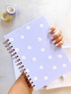 a woman holding a notebook with white flowers on it and the cover is open to show her nails