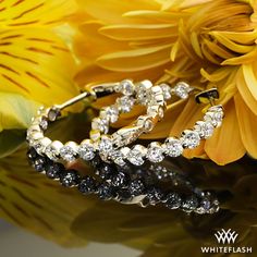 two diamond hoop earrings sitting on top of yellow flowers