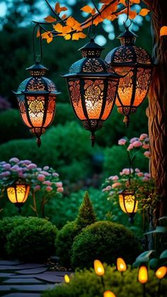 three lanterns hanging from a tree in the middle of a garden with flowers and bushes