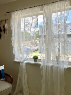 a window with white curtains in front of it and a potted plant next to the window