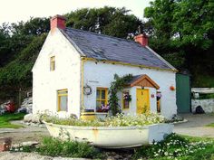 a white house with a yellow door and windows next to a green tree filled field