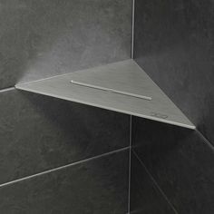 the corner of a shower head is shown in grey tile, with an angled metal shelf above it