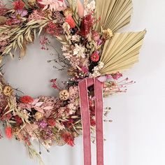 a floral wreath hanging on the wall next to a pink ribbon with flowers and leaves