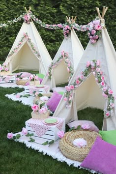 several teepees are set up in the grass with pink flowers and greenery