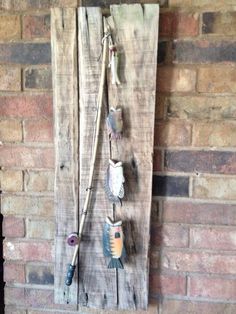 an old wooden wall hanging on the side of a brick building with fish hooks attached to it