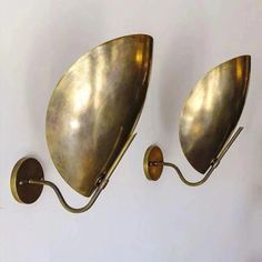 two brass wall lights mounted to the side of a white wall, one is turned upside down