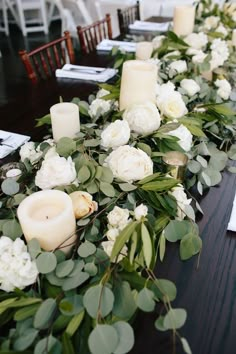 the table is set with candles and flowers on it, along with greenery for decoration