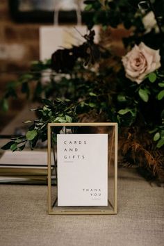 a card and gifts sign sitting on top of a table next to some greenery