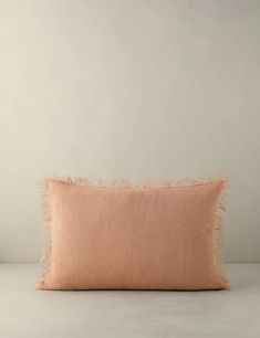 an orange pillow with fringes on the front and back, against a white wall