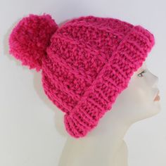 a pink knitted hat with two pompoms on it's sides, sitting on a mannequin head