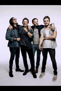 four young men are posing together for a photo in front of a white background, one is holding his arms around the other