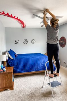 a woman standing on top of a stepladder working on a ceiling fan in a bedroom