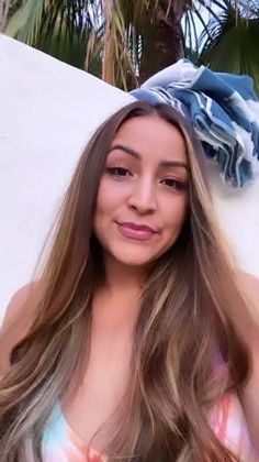 a woman with long hair standing in front of a white wall wearing a tie dye top