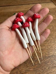 small red and white mushrooms sitting on top of toothpicks in someone's hand