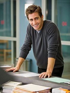 a man leaning over a table with lots of papers on it and smiling at the camera