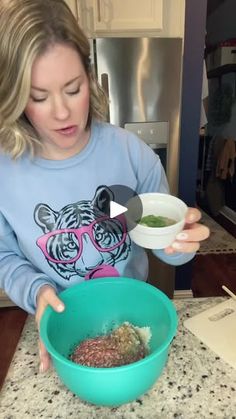 a woman in a blue sweatshirt is mixing food into a bowl