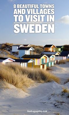 a row of beach huts on the sand with grass in foreground and blue sky above