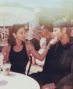 a man sitting next to a woman at a table with an umbrella over her head