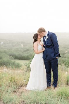 a bride and groom kissing on top of a hill