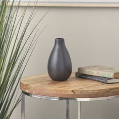 a black vase sitting on top of a wooden table next to a book and plant