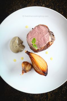 a white plate topped with meat and an onion next to a piece of artichoke