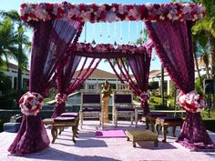 an outdoor wedding setup with purple drapes and pink flowers on the bedding,