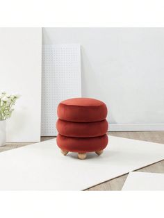 a red ottoman sitting on top of a white rug next to a vase with flowers