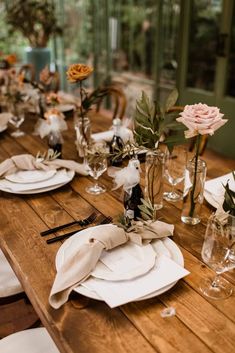 the table is set with white plates and napkins, flowers in vases on each plate