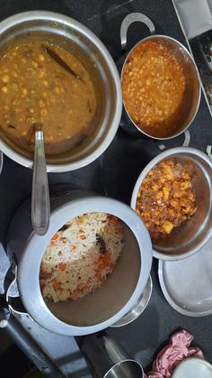 several bowls filled with food on top of a black counter next to utensils