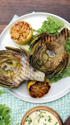 grilled artichokes on a white plate next to a bowl of ranch dressing