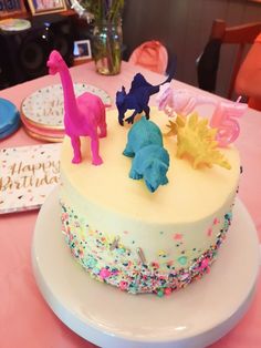 a birthday cake decorated with plastic dinosaurs and sprinkles on a pink table