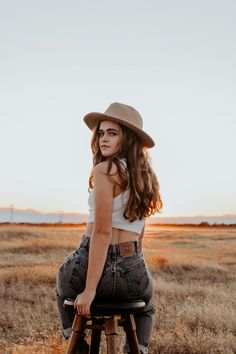 a woman sitting on top of a wooden stool in a field wearing a cowboy hat