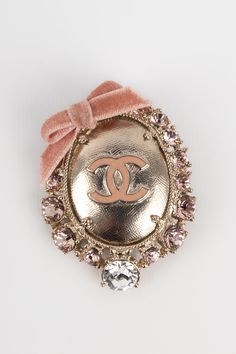 CHANEL - (Made in France) Broche en métal argenté pavée de strass figurant un médaillon surmonté d'un ruban de velours rose. Condition : Très bon état Dimensions : 6 cm x 4,5 cm Ysl Shoes, Chanel Chanel, Dior Shoes, Fendi Bags, Prada Bag, Dior Bag, Made In, Chanel Bag, Gucci Bag