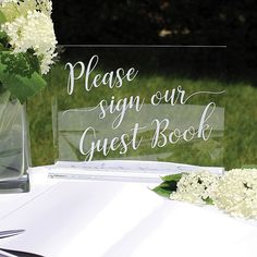 a clear acrylic sign sitting on top of a table next to white flowers