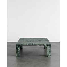 a green marble coffee table sitting on top of a cement floor next to a white wall