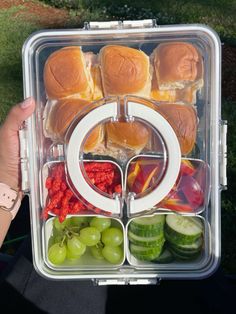 a lunch box with sandwiches, grapes and cucumbers in it is held by a person