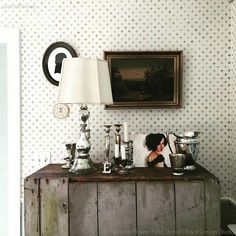 a woman sitting on top of a wooden table next to a lamp and pictures hanging on the wall